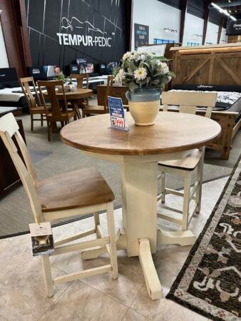 Round wood dining table with two cream-colored chairs on sale.