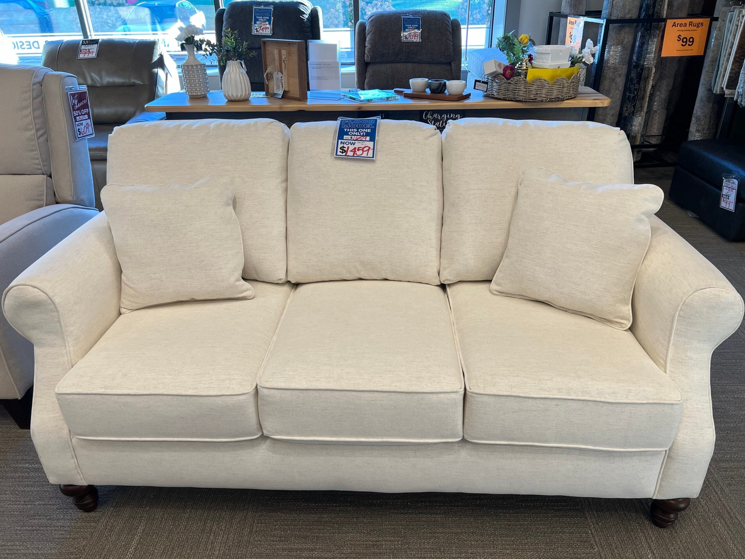 img_0046 Cream three-cushion sofa with rolled arms in a showroom.